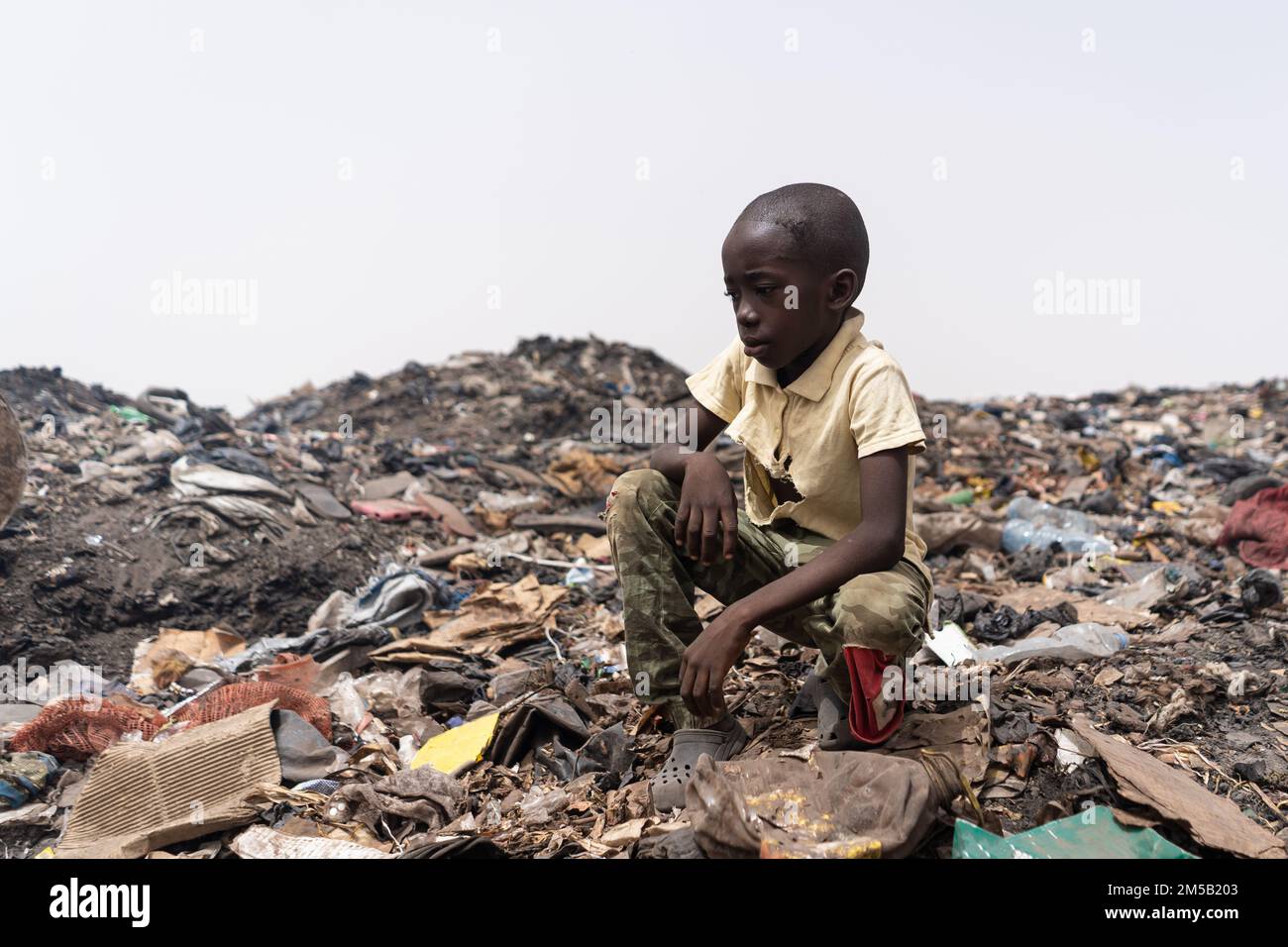 Little African boy surrounded by heaps of household litter; Concept of unsolved waste management in third world countries Stock Photo