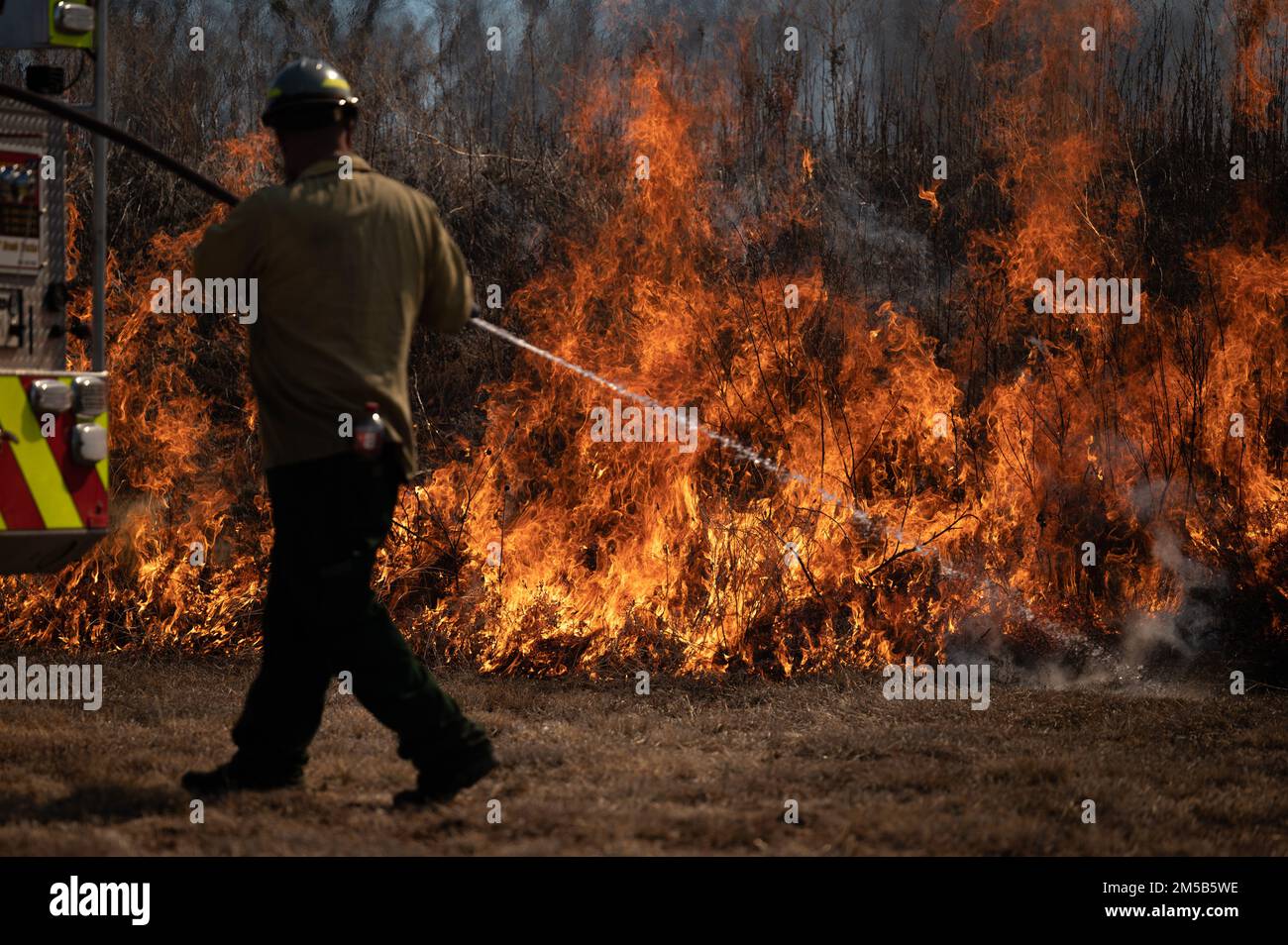 A member of the Air Force Wildland Fire Branch sprays a prescribed wildland brush fire at Dyess Air Force Base, Texas, Feb. 18, 2022. Dyess firefighters and Air Force Wildland firefighters are executing prescribed burns in order to reintroduce fire into the installation’s ecosystem and, as nearly as possible, allow a fire to function in its natural ecological role. Stock Photo