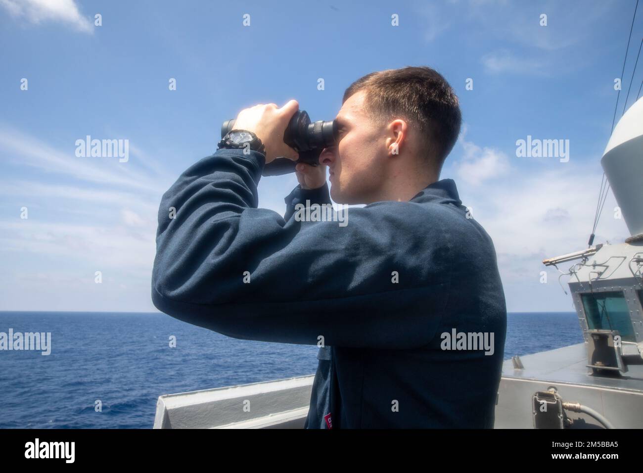 SOUTH CHINA SEA (Feb. 18,2022) Ensign Vince Smetona, from San Clemente, Calif., looks for surface contacts on the bridge wing as the Arleigh Burke-class guided-missile destroyer USS Ralph Johnson (DDG 114) conducts routine underway operations. Ralph Johnson is forward-deployed to the U.S. 7th Fleet area of operations in support of a free and open Indo-Pacific. Stock Photo