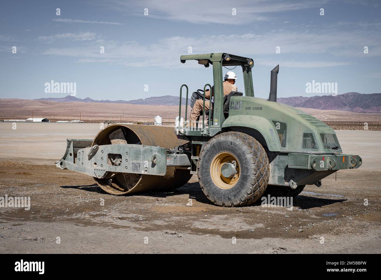 A U.S. Marine with Aviation Ground Support Detachment, Marine Air Ground Task Force Training Command, operates a CS-563D AW Vibratory Single Drum Compactor at the Strategic Expeditionary Landing Field aboard Marine Corps Air Ground Combat Center, Twentynine Palms, California, Feb. 18, 2022. Due to erosion and routine use, periodic maintenance is required on the SELF to ensure the subgrade underneath the AM-2 aluminum matting remains within safety criteria. Stock Photo