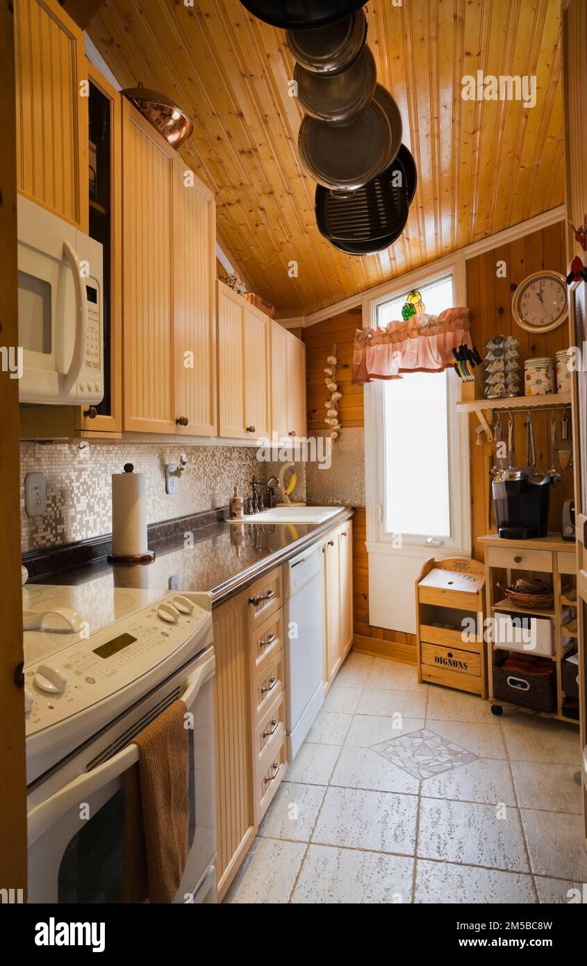 Bleached maple wood cabinets, pine wood plank wall and ceiling, travertine ceramic tile floor in kitchen inside 1987 Archimed style home. Stock Photo
