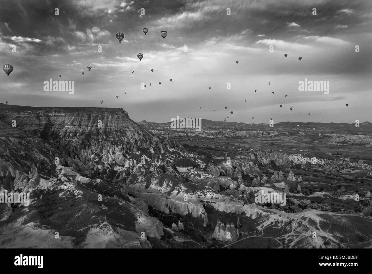 A breathtaking view of the Pasabag Valley in Cappadocia, Turkey, with beautiful nature, with hot-air balloons flying above the valley, in a grayscale Stock Photo