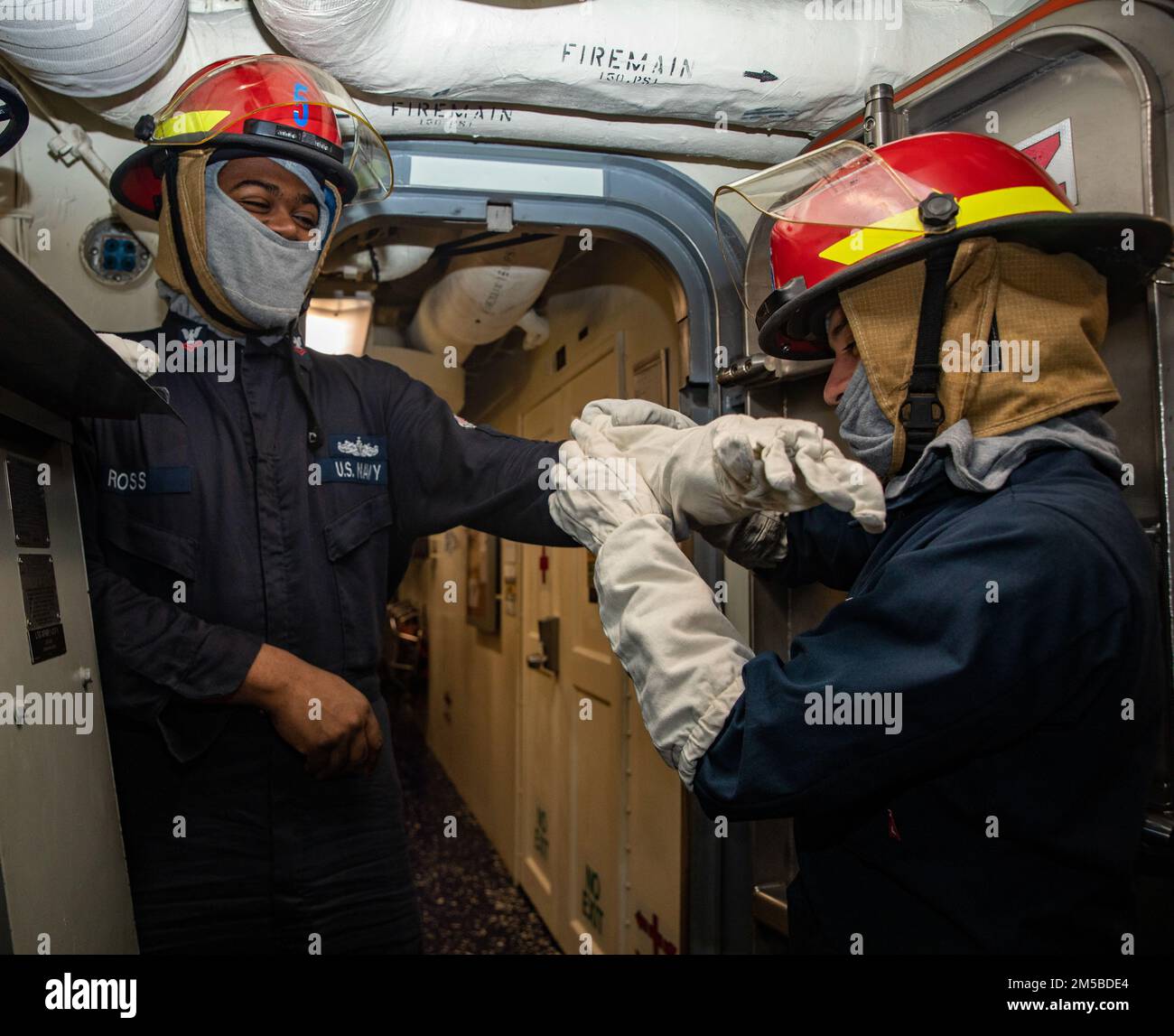 SOUTH CHINA SEA (Feb. 19, 2022) Gas Turbine Systems Technician (Mechanical) Fireman Aaron Ledesma (right), from Castroville, Texas, helps Gas Turbine Systems Technician (Mechanical) 2nd Class Maurice Ross (left), from Columbus, Ohio don flash gear during a damage control drill aboard Arleigh Burke-class guided-missile destroyer USS Ralph Johnson (DDG 114). Ralph Johnson is assigned to Task Force 71/Destroyer Squadron (DESRON) 15, the Navy’s largest forward-deployed DESRON and the U.S. 7th fleet’s principal surface force. Stock Photo