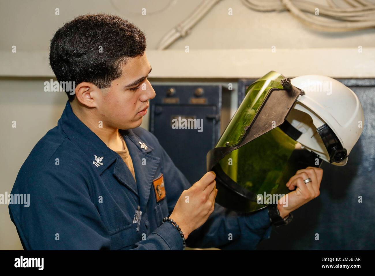PHILIPPINE SEA (Feb. 22, 2022) Electrician’s Mate 2nd Class Erick Cobos, from Miami, inspects a face shield prior to initial voltage verification aboard the Nimitz-class aircraft carrier USS Abraham Lincoln (CVN 72). Abraham Lincoln Strike Group is on a scheduled deployment in the U.S. 7th Fleet area of operations to enhance interoperability through alliances and partnerships while serving as a ready-response force in support of a free and open Indo-Pacific region. Stock Photo