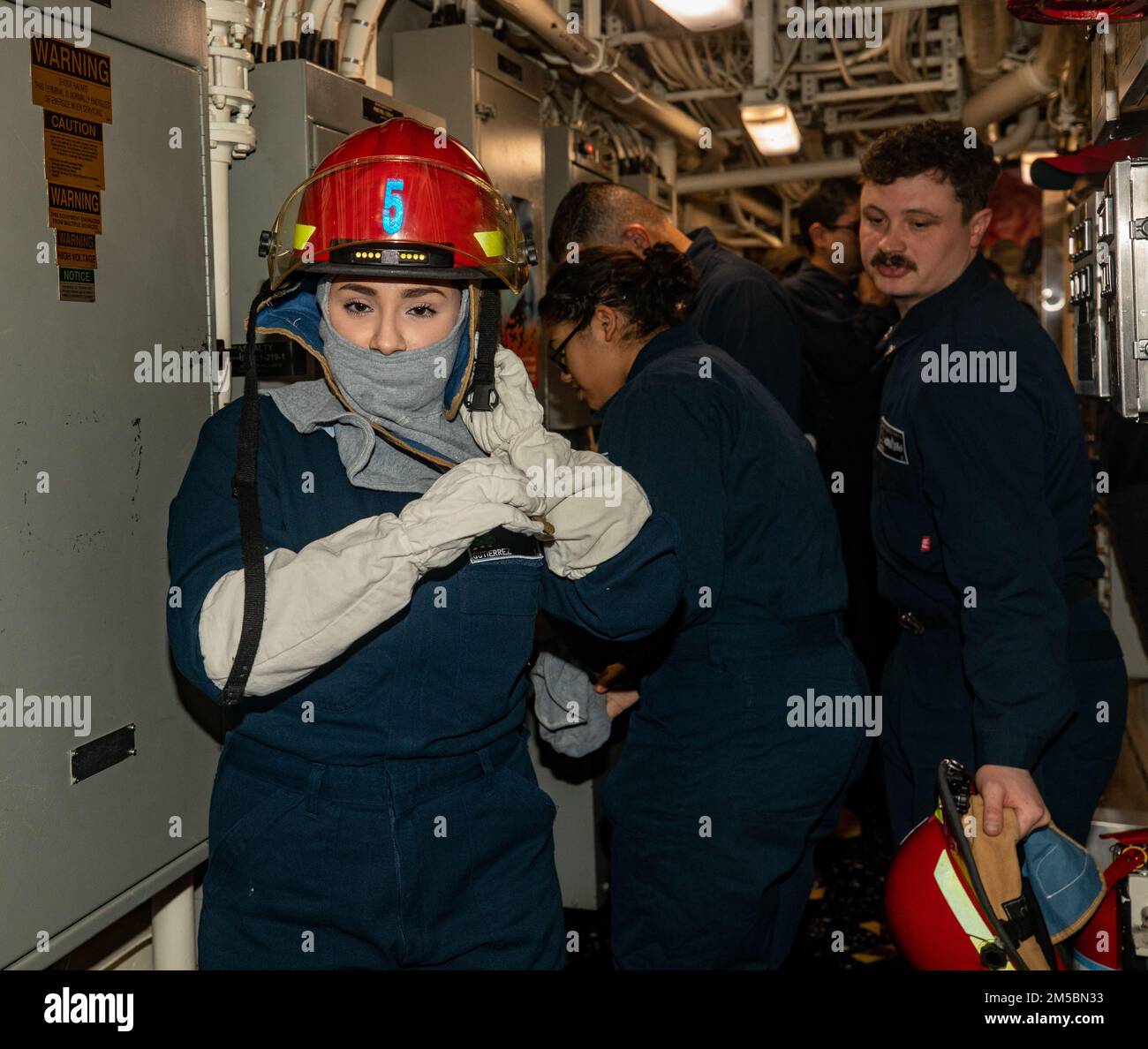 SOUTH CHINA SEA (Feb. 23, 2022) Sailors don flash gear during a damage control drill aboard Arleigh Burke-class guided-missile destroyer USS Ralph Johnson (DDG 114). Ralph Johnson is assigned to Task Force 71/Destroyer Squadron (DESRON) 15, the Navy’s largest forward-deployed DESRON and the U.S. 7th fleet’s principal surface force. Stock Photo
