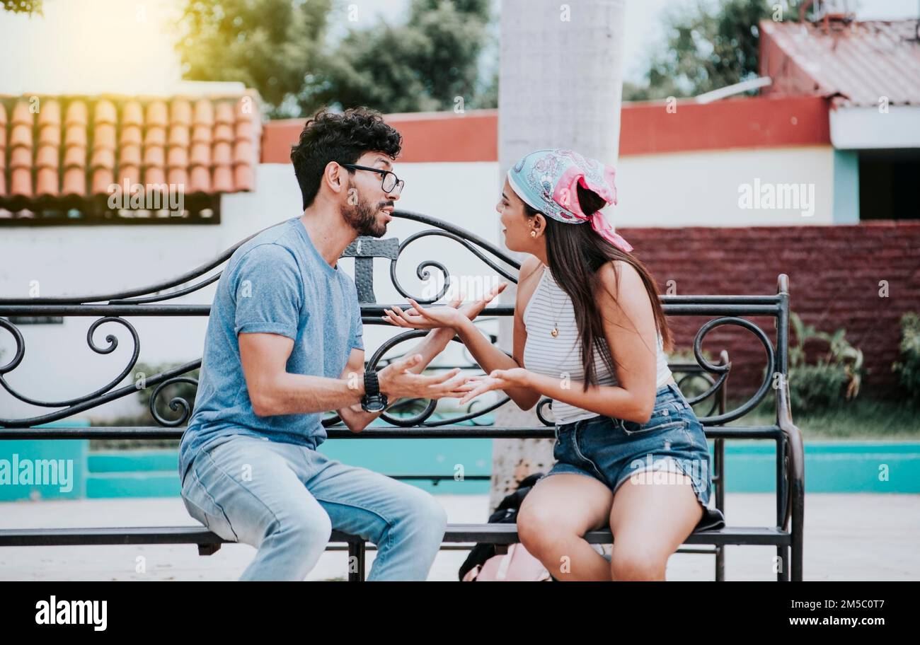 Man arguing with his girlfriend sitting in a park. Young couple arguing sitting on a park bench, Concept of aggressive couples in the park. Upset Stock Photo