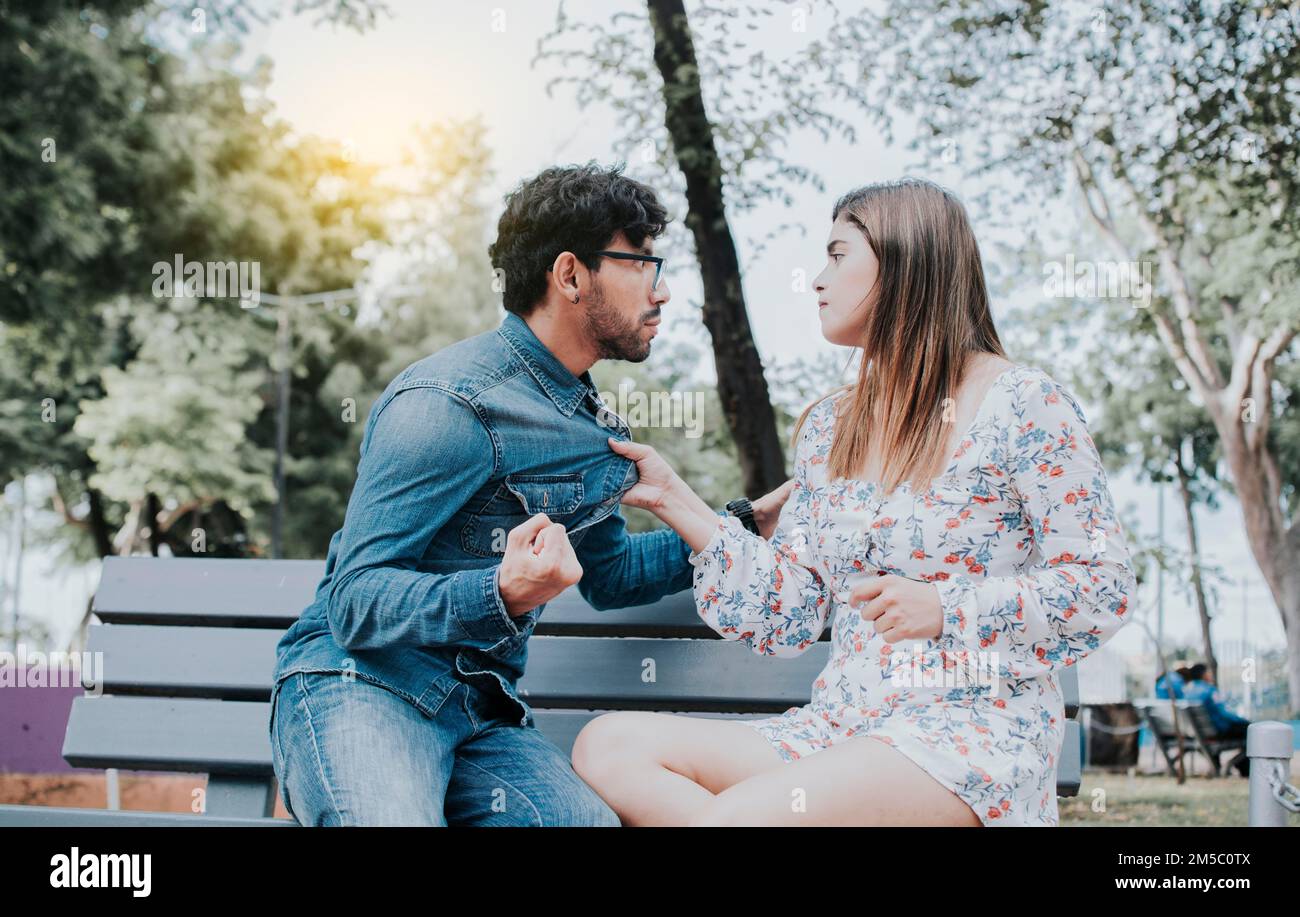Upset couple arguing on a park bench. Young couple arguing sitting on a park bench, Concept of aggressive couples in the park. Man arguing with his Stock Photo