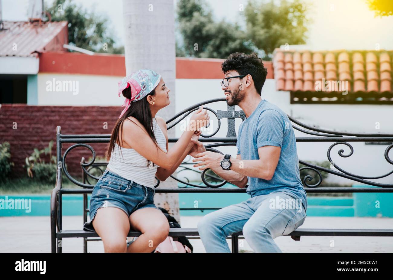 Young couple arguing sitting on a park bench, Concept of aggressive couples in the park. Upset couple arguing on a park bench. Man arguing with his Stock Photo