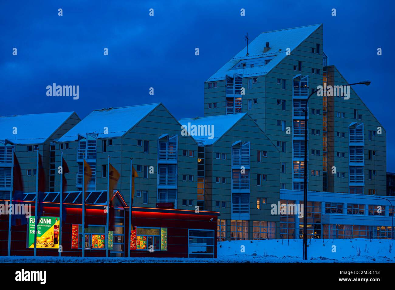 Illuminated supermarket at dawn, behind it apartment buildings in ...