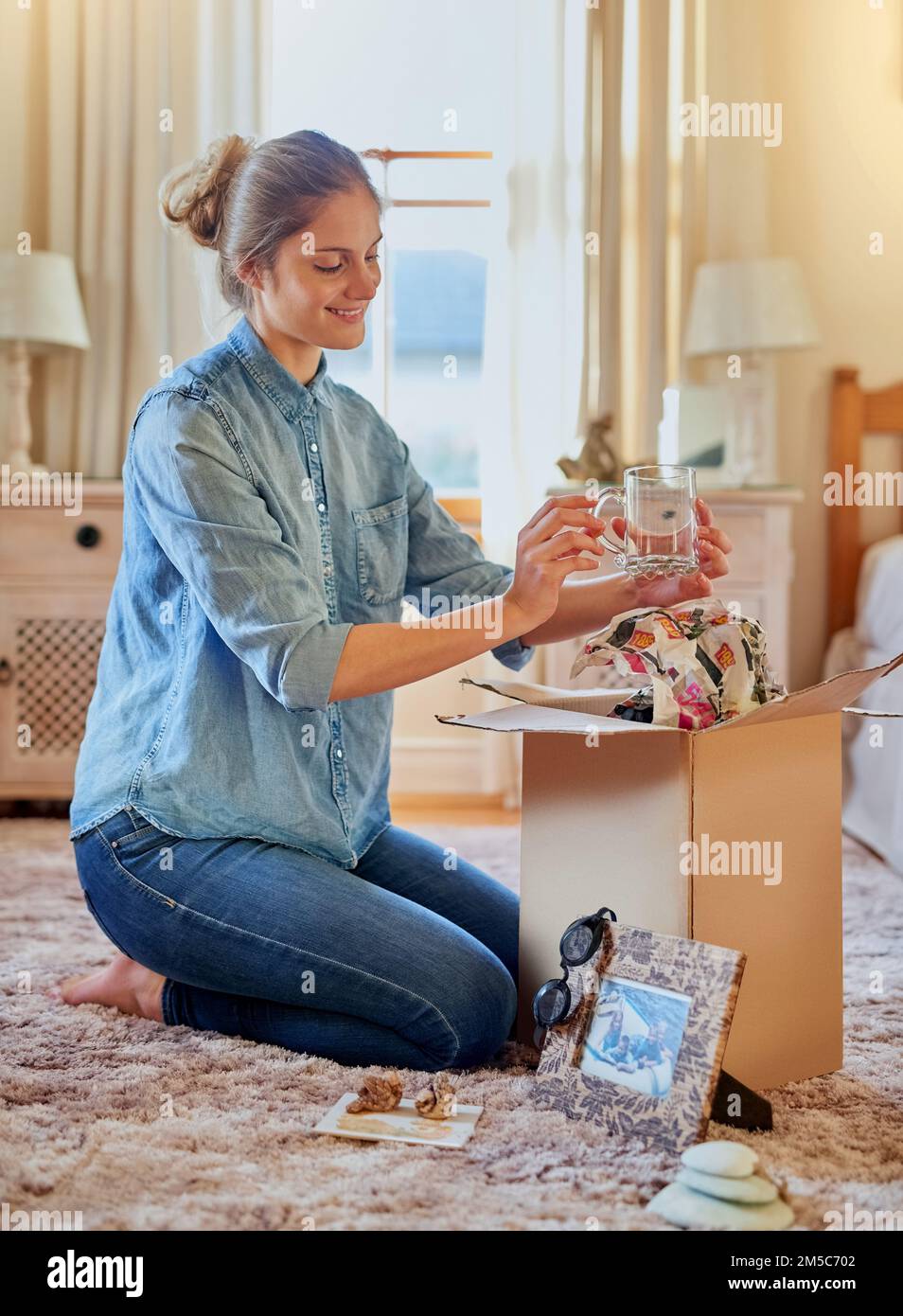 Taking a trip down memory lane. a young woman unpacking a box at home. Stock Photo