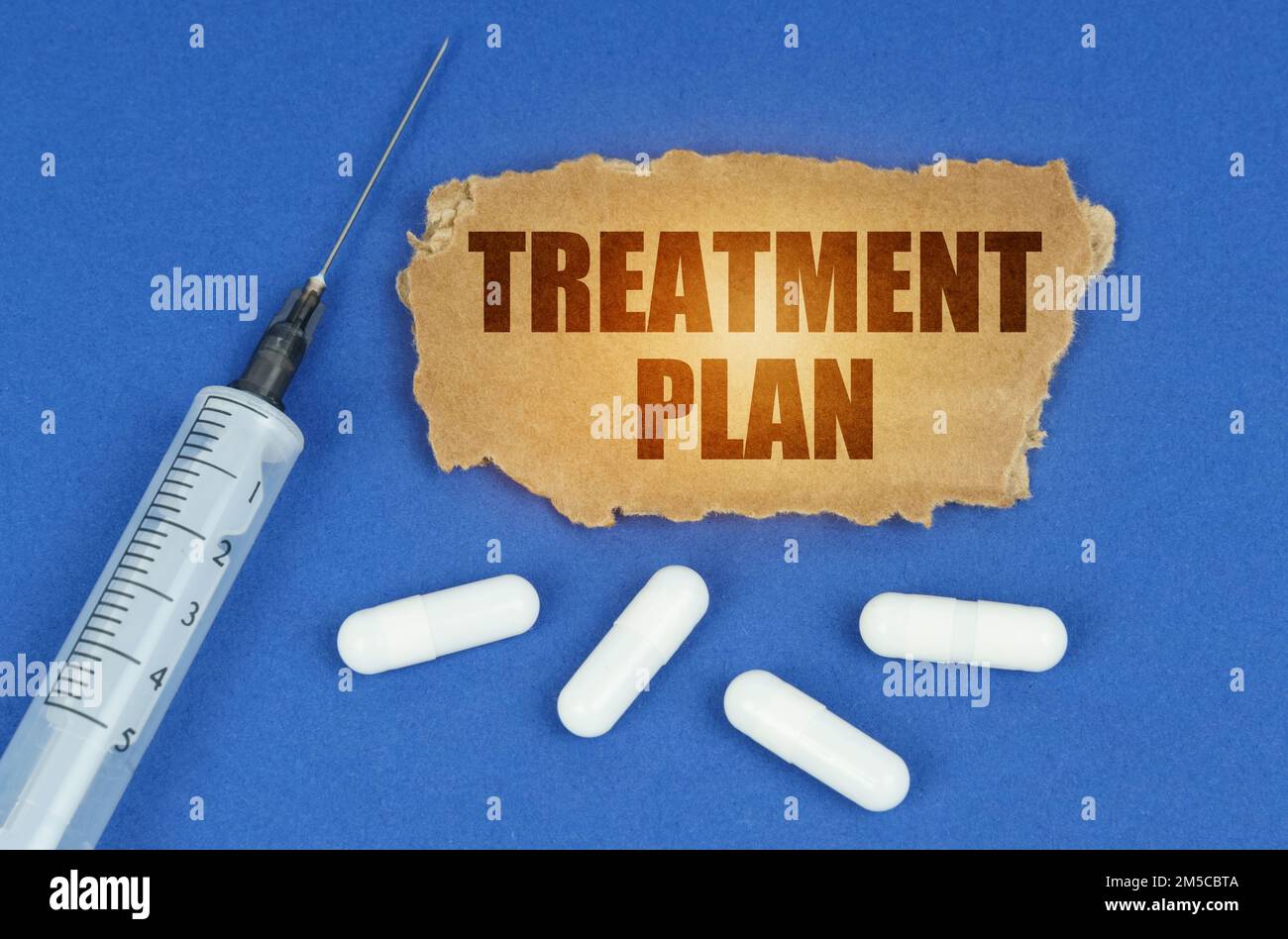 Medical concept. On a blue surface lie a syringe, pills and a cardboard sign with the inscription - TREATMENT PLAN Stock Photo