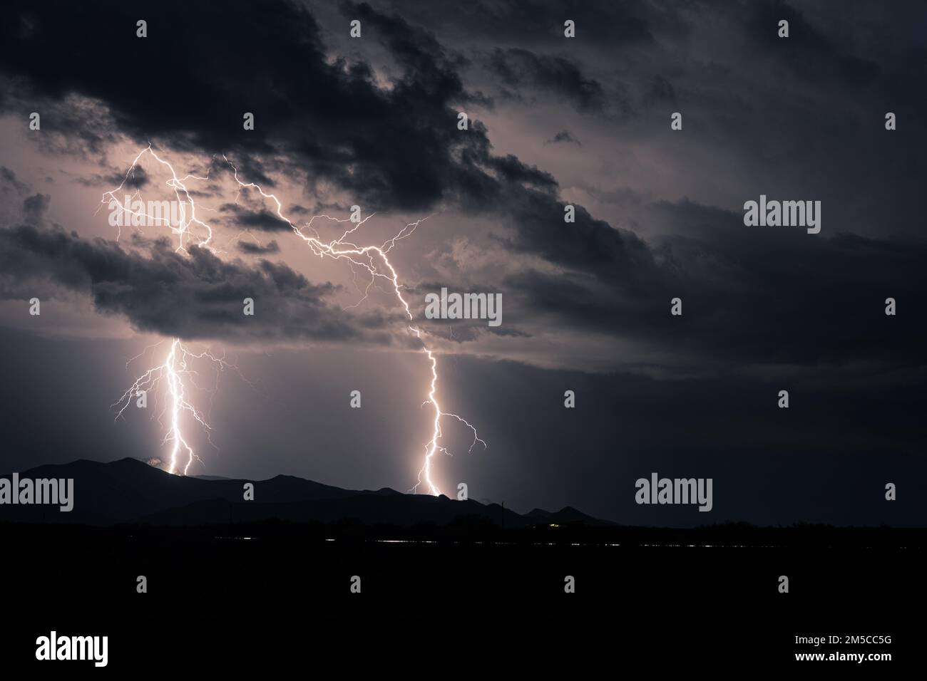 A huge storm over distant mountains with bolts of lightning flashing across the sky Stock Photo