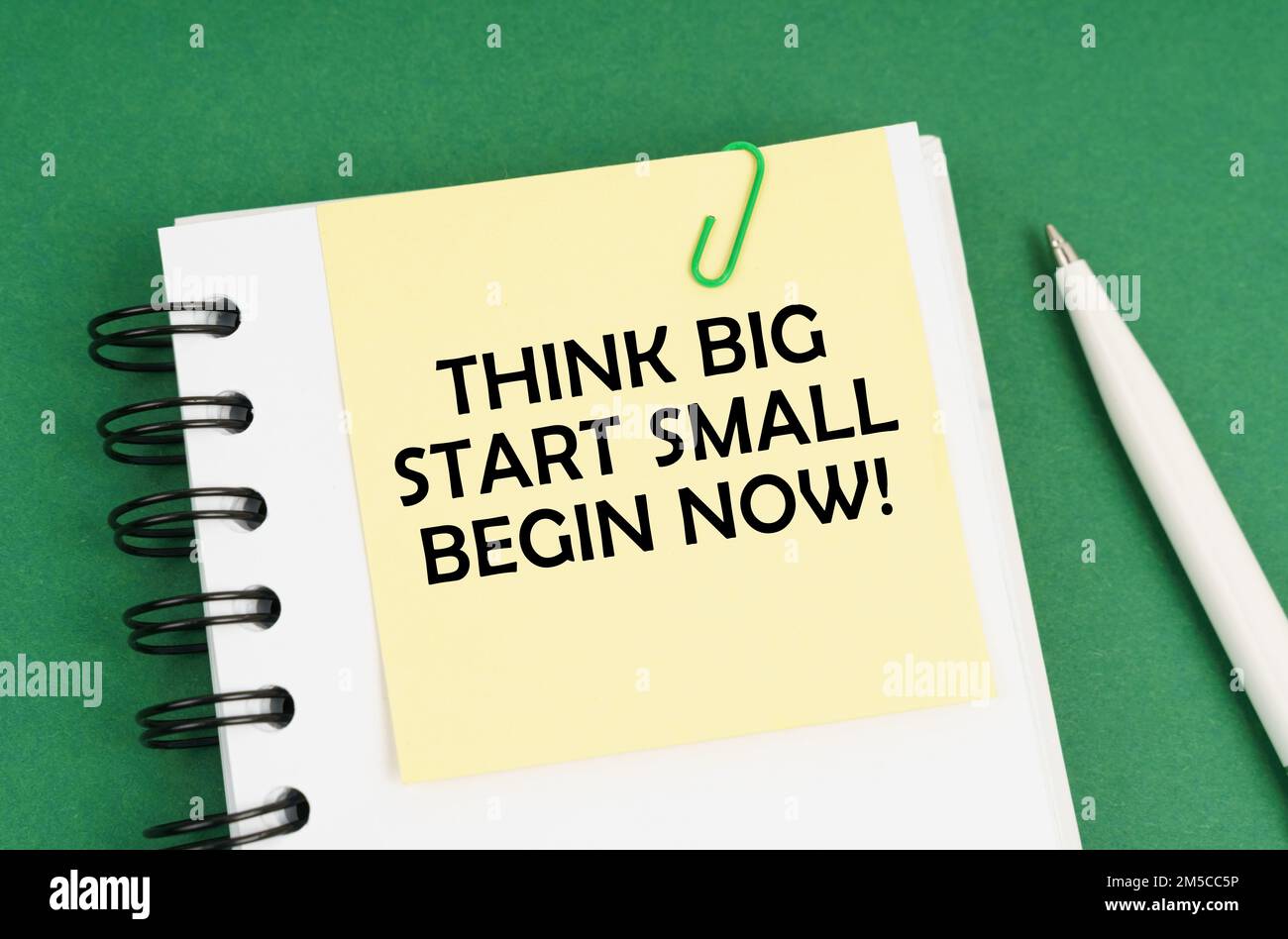 Business concept. On a green surface, a pen, a notepad with stickers and the inscription - Think Big Start Small Begin Now Stock Photo