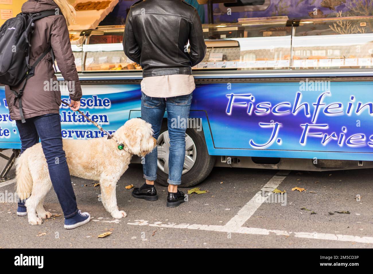 Two people waiting in line for fish and chips with white dog on a leash and black outfits Stock Photo