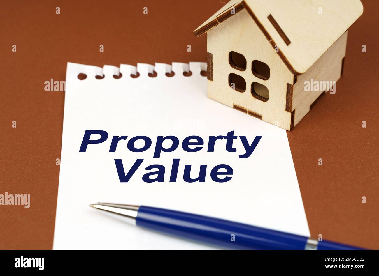 Business concept. On a brown surface is a house, a pen and a notepad with the inscription - Property Value Stock Photo