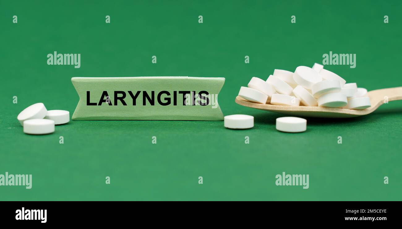 Medicine concept. On a green surface, a wooden spoon with pills and a sign with the inscription - Laryngitis Stock Photo