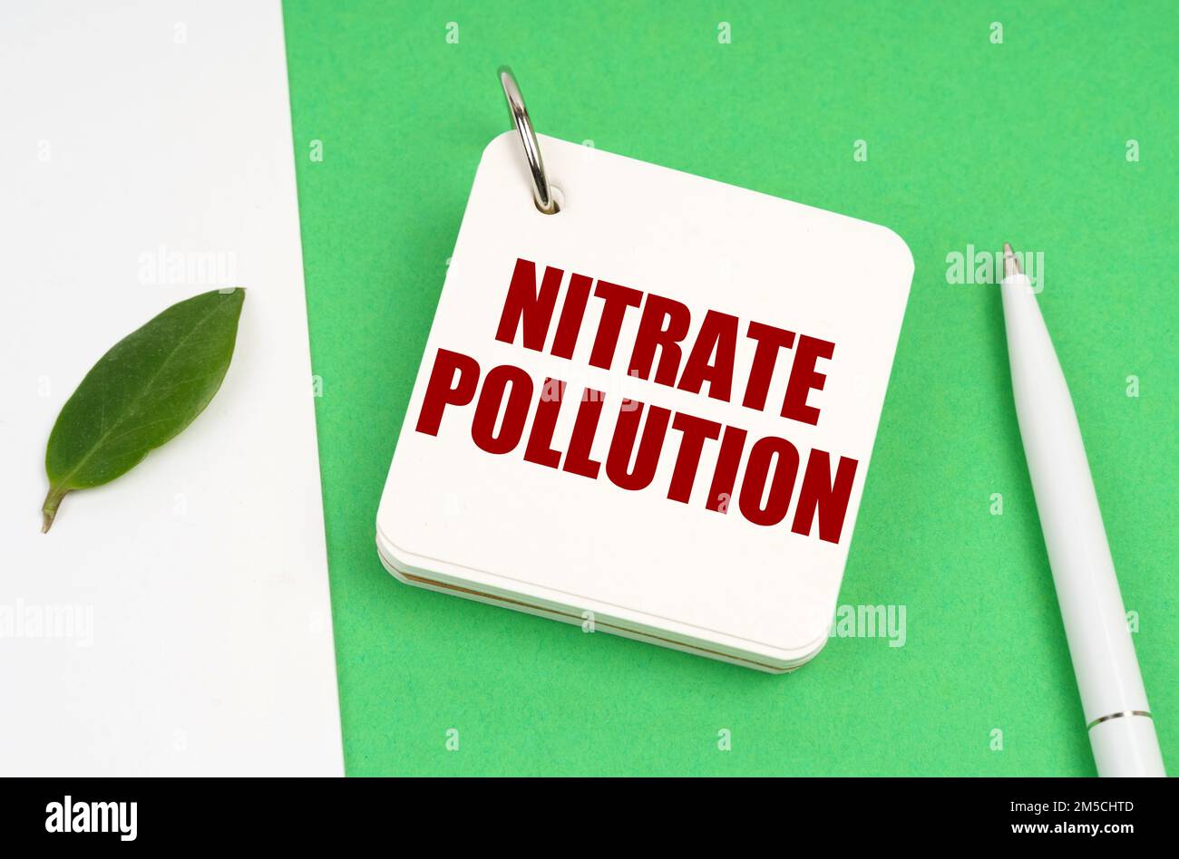 Ecological concept. On a white-green surface, a piece of paper, a pen and a notepad with the text - nitrate pollution Stock Photo