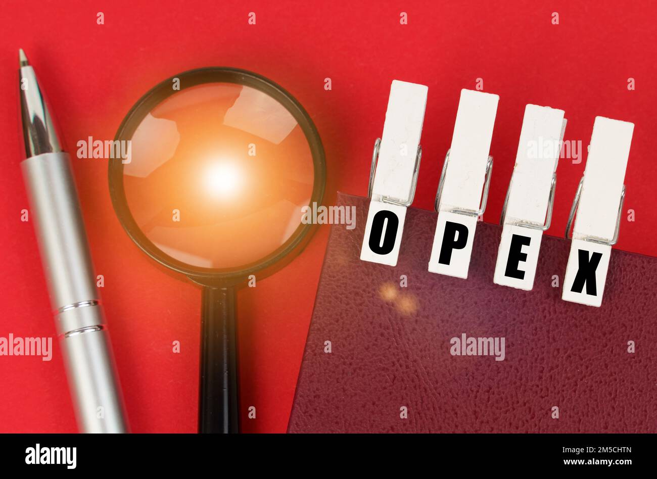 Business concept. On the red surface there is a magnifying glass, a notepad and clothespins with the inscription - OPEX Stock Photo