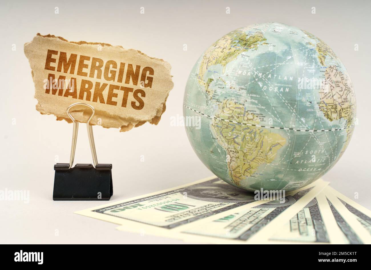Business concept. On a gray surface, a globe, dollars and a cardboard plate with the inscription - EMERGING MARKETS Stock Photo