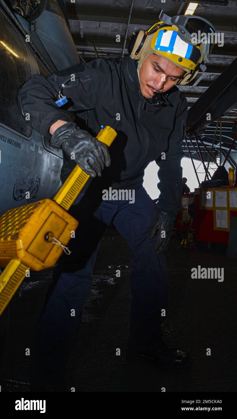 220302-N-GP384-1039 NORTH AEGEAN SEA (Mar. 2, 2022) Aviation Boatswain's Mate (Handling) Airman Damyan Mendoza, from Santa Clara, California, removes a chock from an MH-60S Sea Hawk, attached to the 'Dragonslayers' of Helicopter Sea Combat Squadron (HSC) 11, in the hangar bay of the Nimitz-class aircraft carrier USS Harry S. Truman (CVN 75), Mar. 2, 2022. The Harry S. Truman Carrier Strike Group is on a scheduled deployment in the U.S. Sixth Fleet area of operations in support of U.S., allied and partner interests in Europe and Africa. Stock Photo