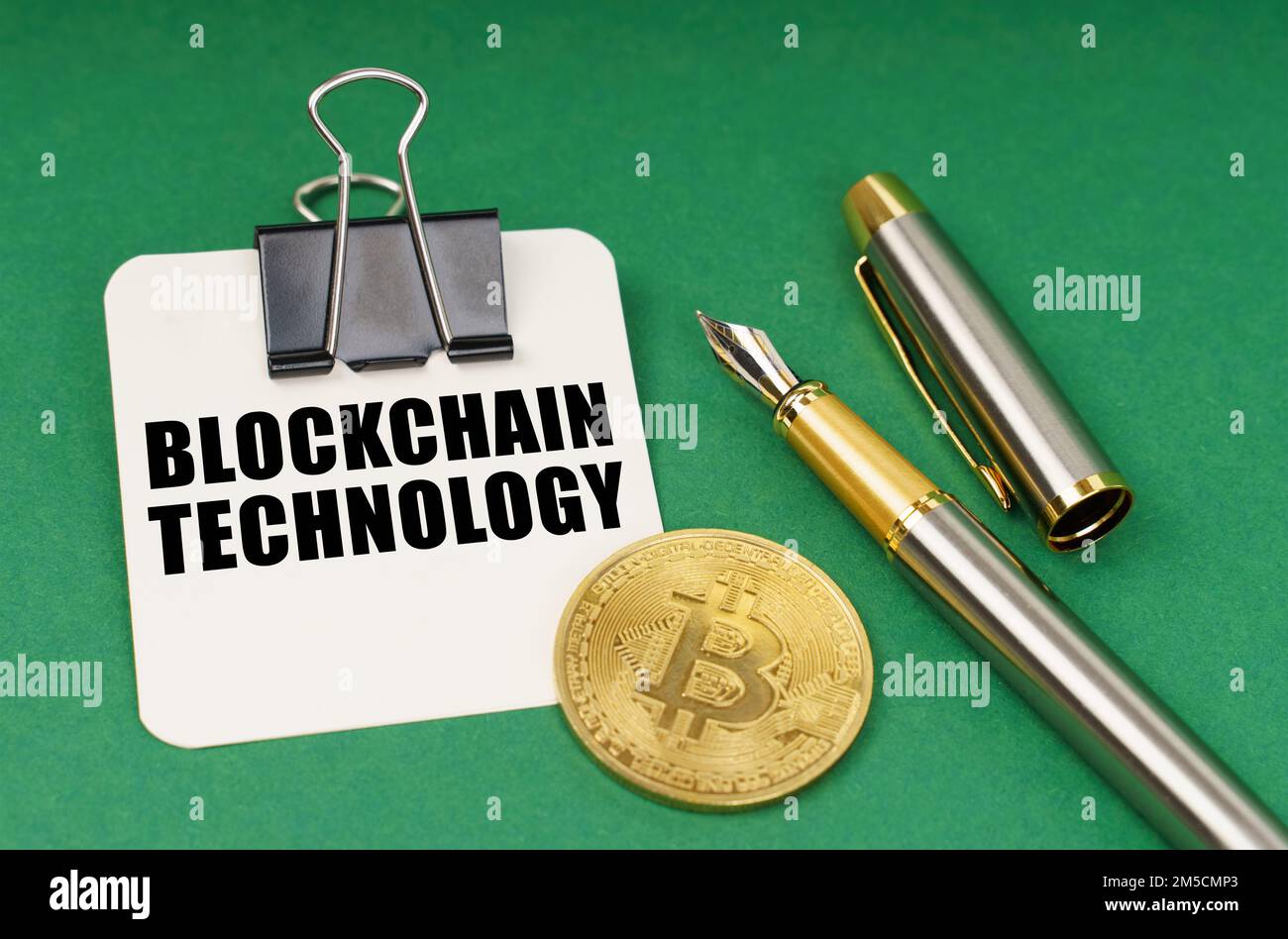 Cryptocurrency and business concept. On a green surface, a bitcoin coin, a pen and a sheet of paper with the inscription - Blockchain technology Stock Photo