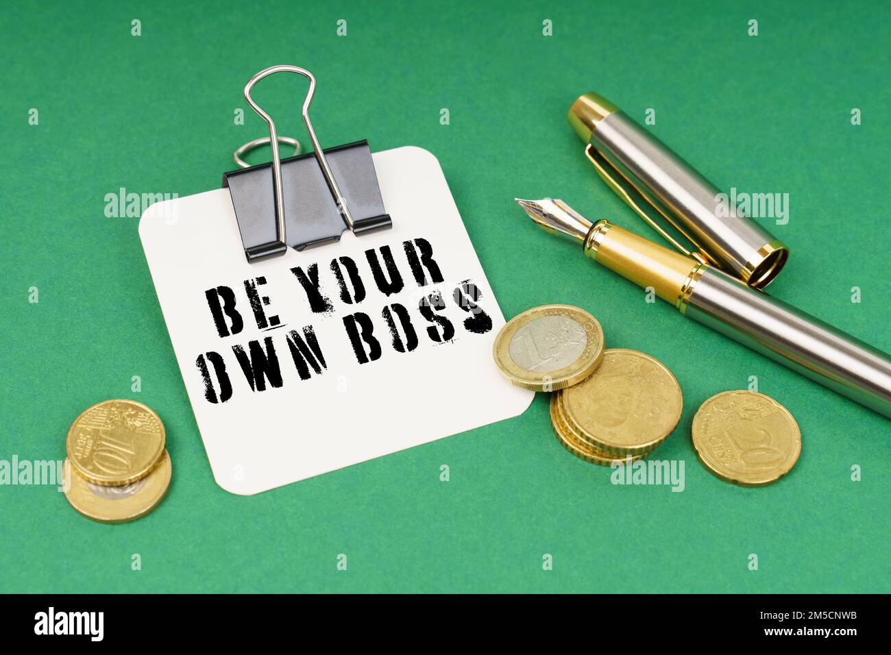 Business and finance concept. On a green surface, a pen, coins and a notepad with the inscription - Be Your Own Boss Stock Photo