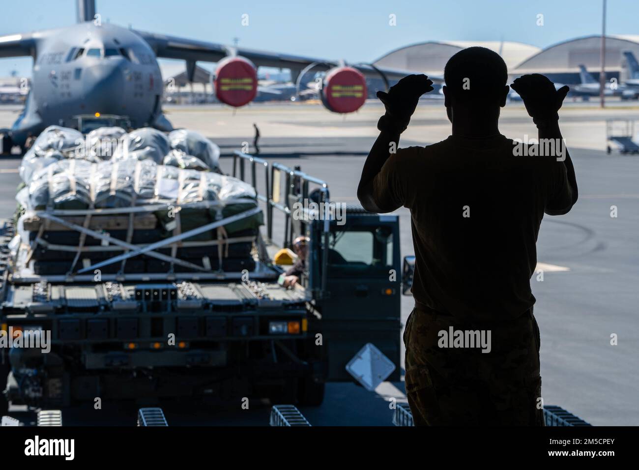 Airman 1st Class Jovanni Bauchi, 535th Airlift Squadron loadmaster, directs a Tunner 60K aircraft cargo loader/transporter transporting cargo onto a C-17 Globemaster III during Exercise TROPIC FURY at Joint Base Pearl Harbor-Hickam, Hawaii, March 2, 2022. The first phase of the exercise emphasizes JBPHH Air Force readiness to combat future operations in the Pacific region by showing its capability to deploy equipment and aircraft anytime, anywhere. Stock Photo