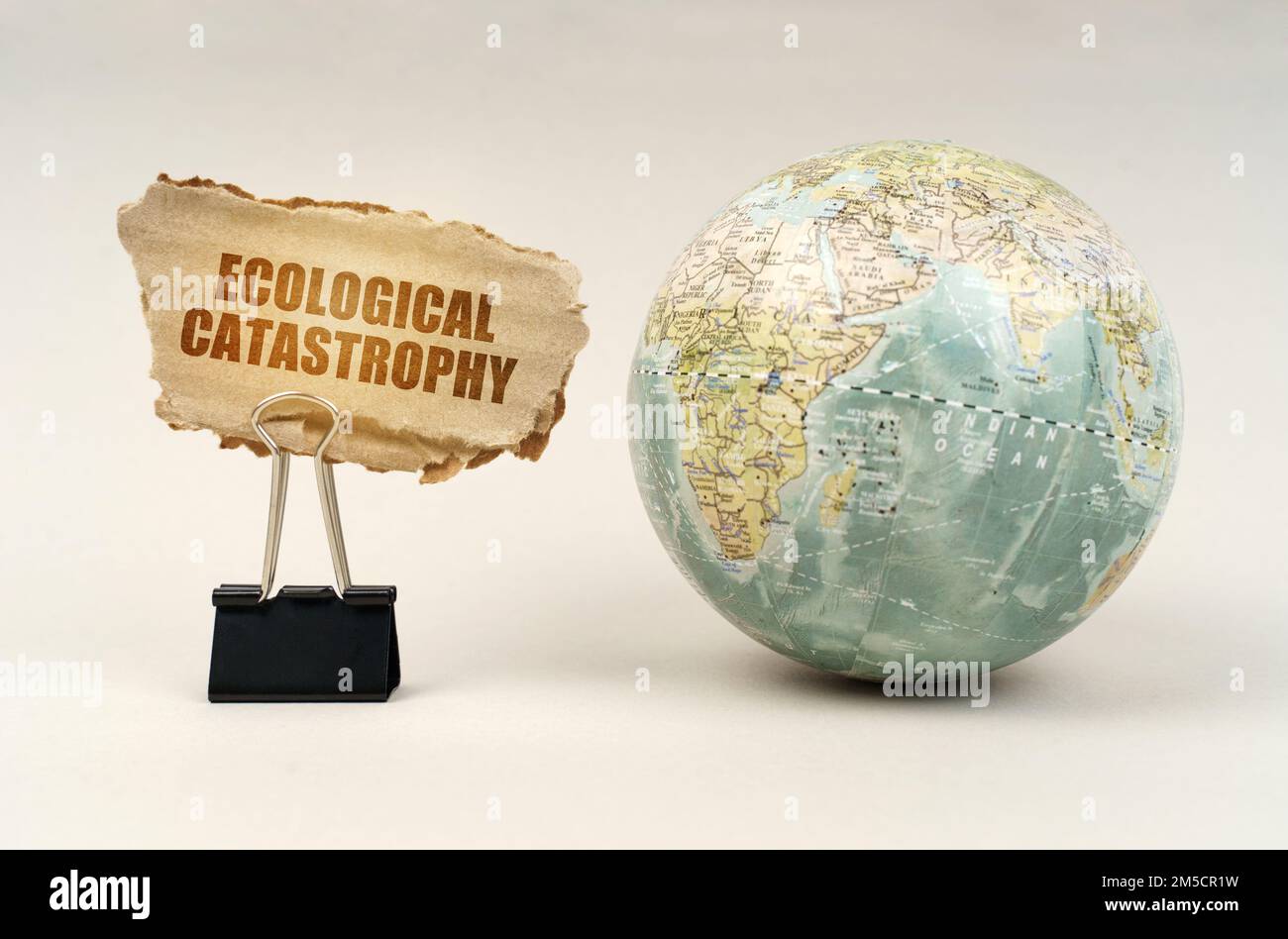 Ecological concept. Near the globe there is a clip with a cardboard plate on which it is written - Ecological catastrophy Stock Photo