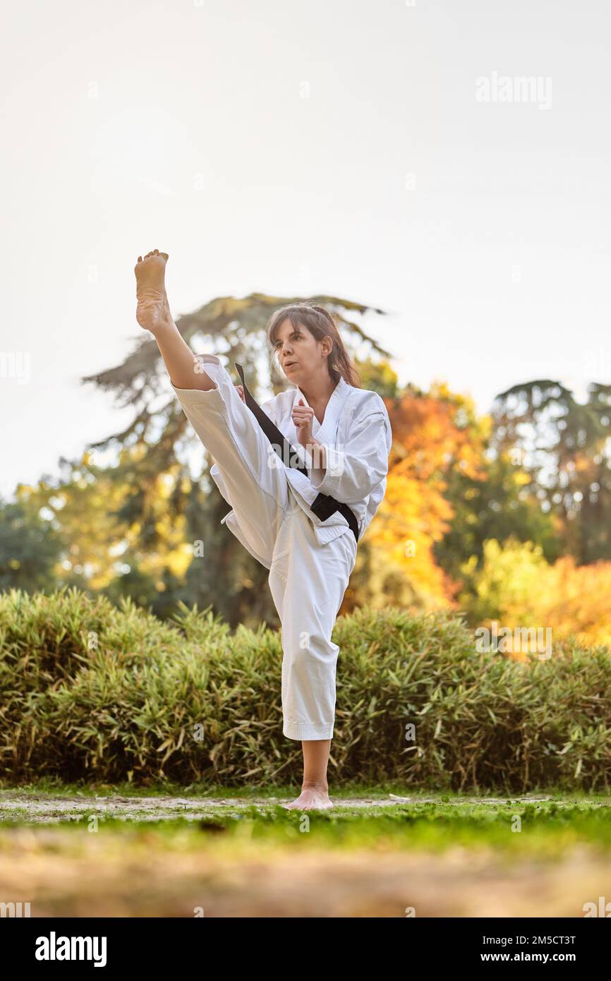 Fighter woman in kimono and black belt standing in karate position outdoors in nature. Sports and martial arts concept. Stock Photo