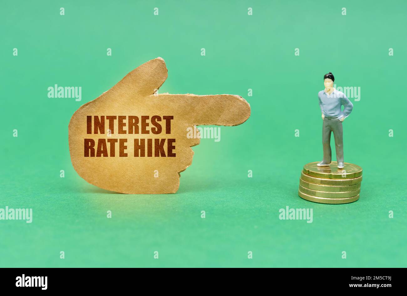 Business concept. On the green surface on the coins there is a figure of a man, a hand with the inscription points to him - Interest rate hike Stock Photo