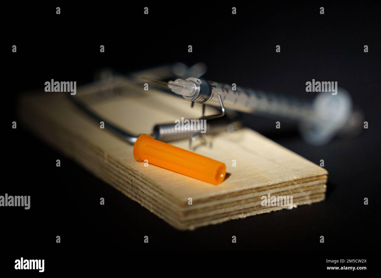 Disposable insulin syringe lying in a wooden mousetrap on a black