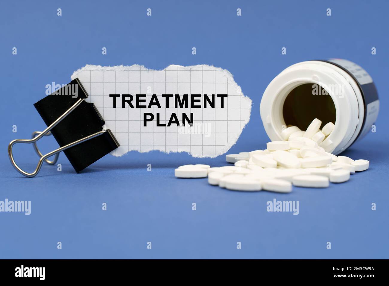 Medicine concept. On the blue surface lies a jar of pills and a clip with paper on which is written - TREATMENT PLAN Stock Photo