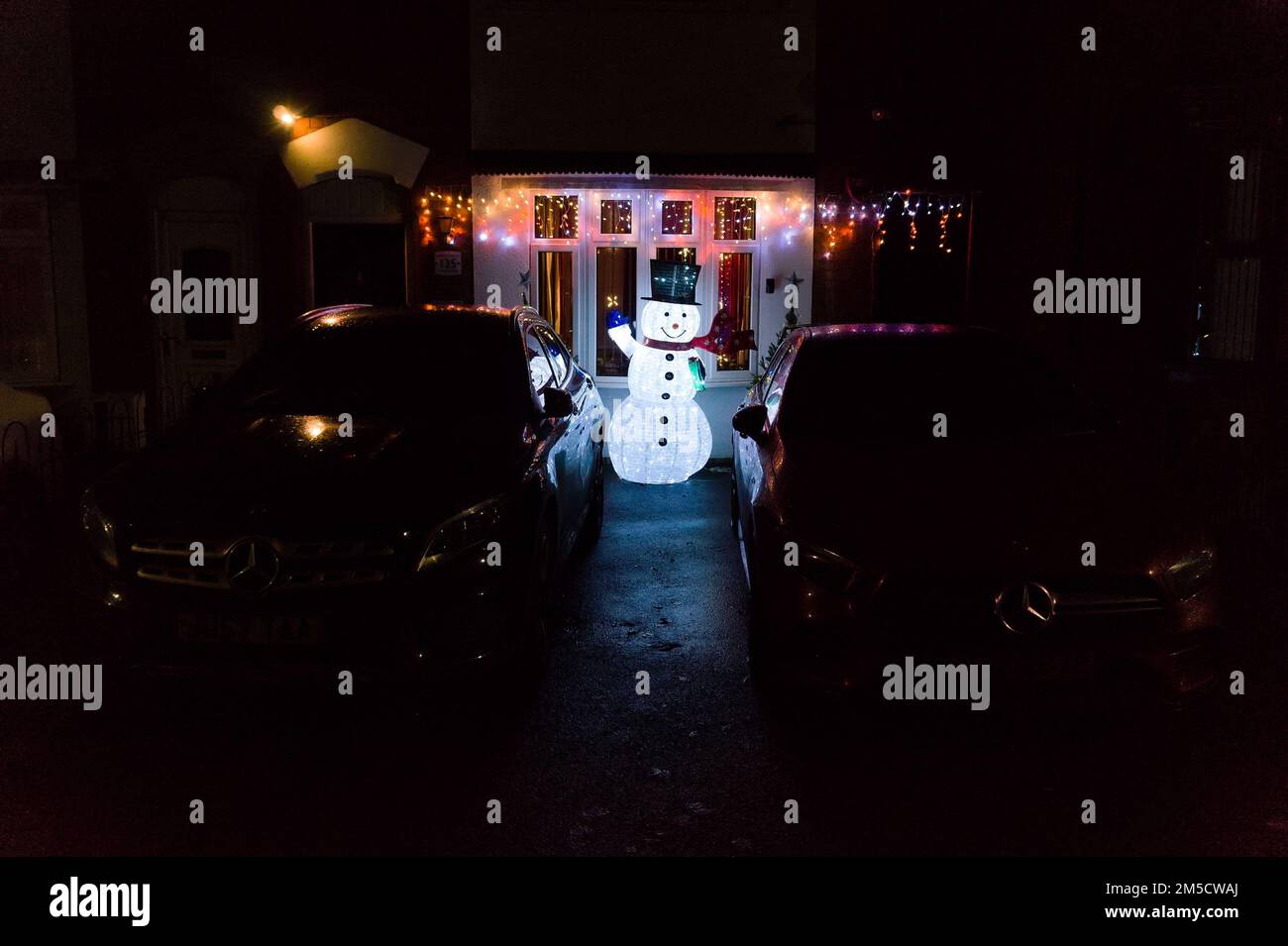 Illuminated snowman statue and Christmas lights in a driveway outside a house at night Stock Photo
