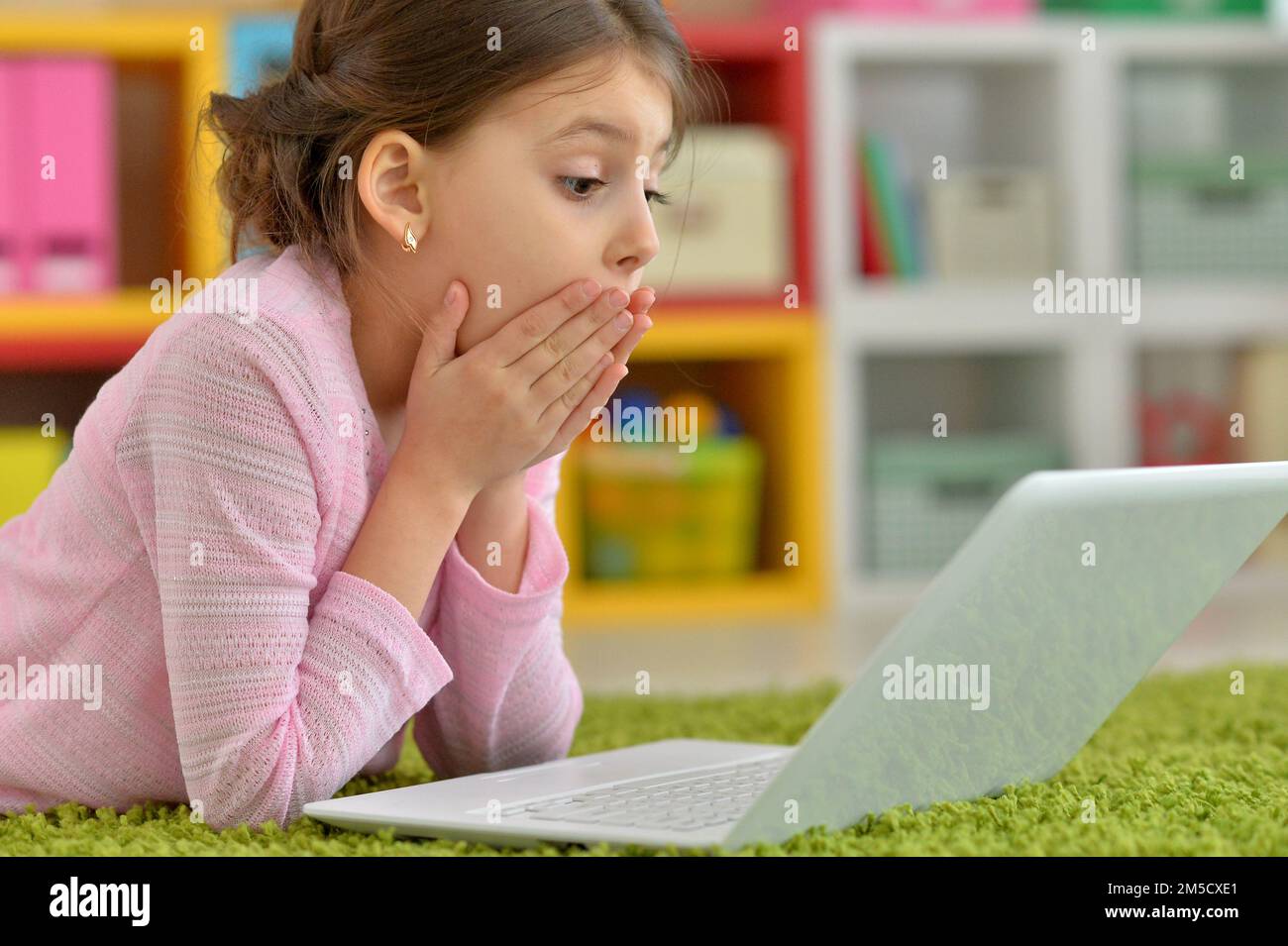 Emotional cute girl using laptop while lying on floor Stock Photo - Alamy