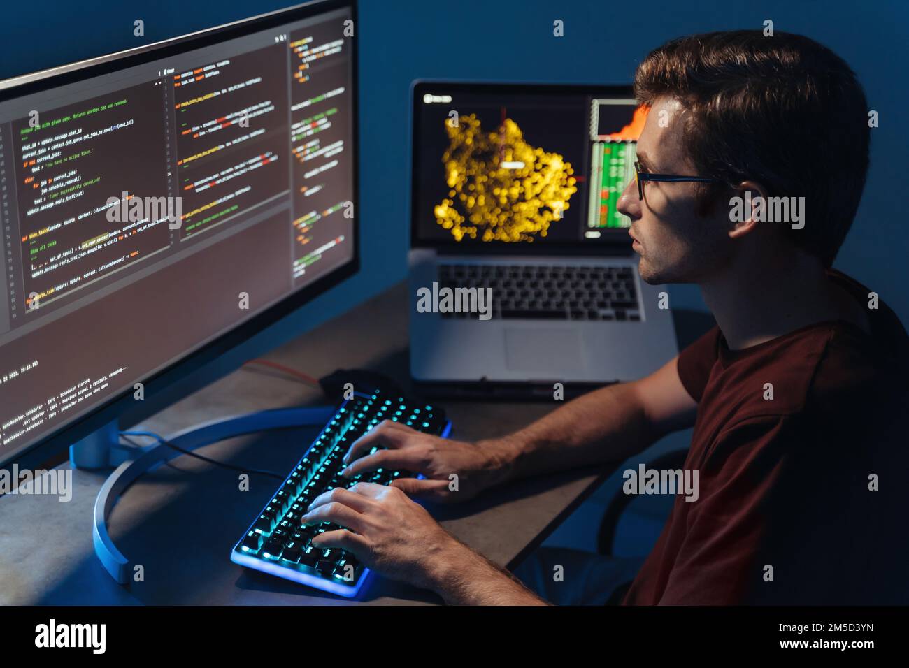 Profile closeup view of young handsome program developer writing software on multiple computer screens at home office. IT specialist, data scientist, coding concept Stock Photo