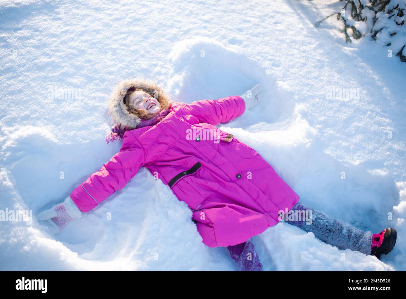 Cute smiling child girl 56 year old lying in snow making angel shape