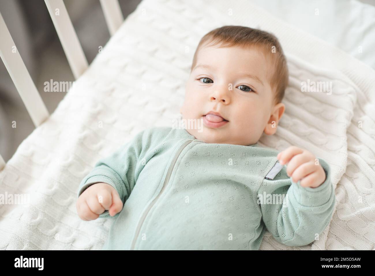 Funny smiling infant baby boy wake up in bed crib look at camera