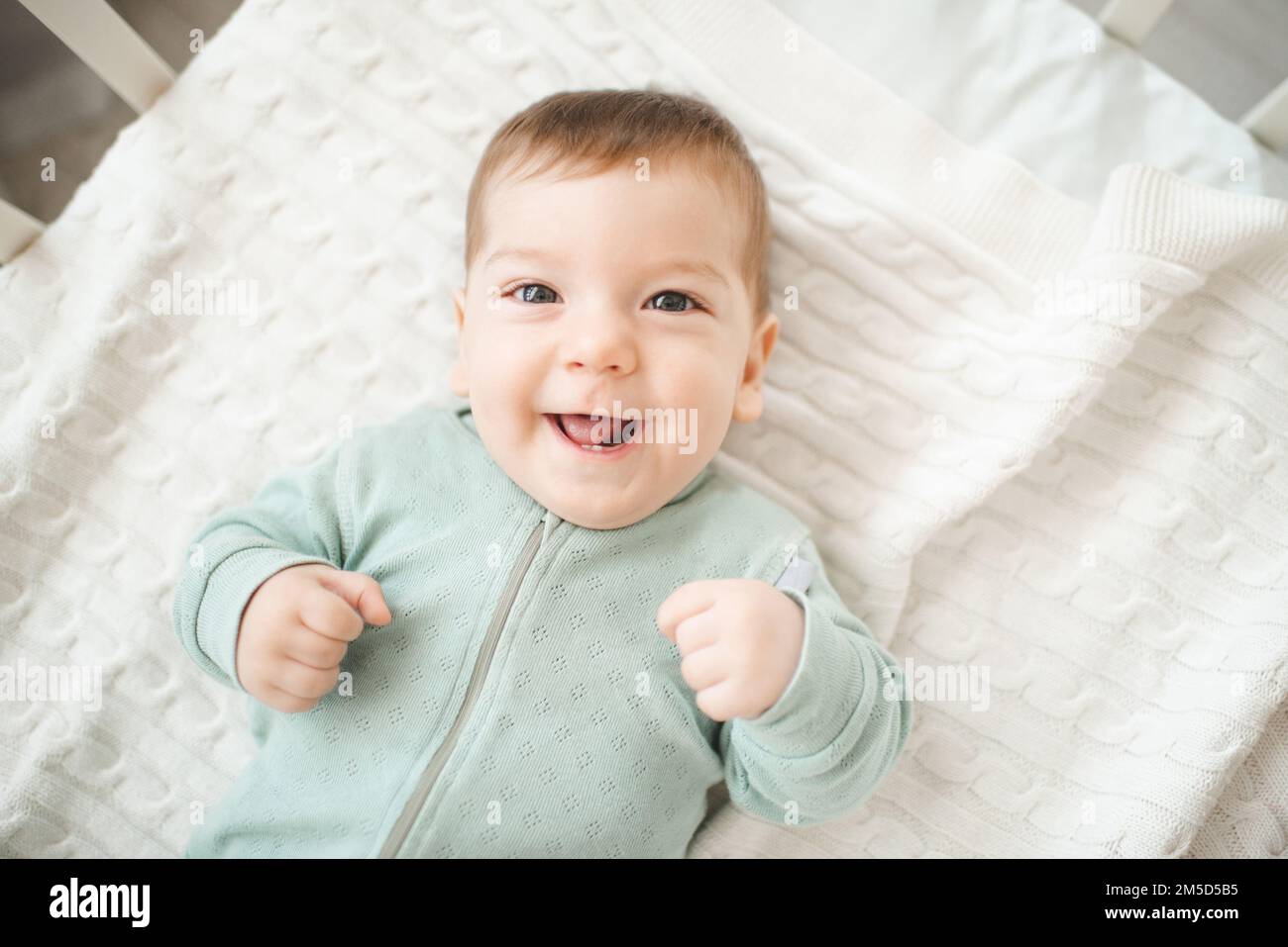 Funny smiling infant baby boy wake up in bed crib look at camera over