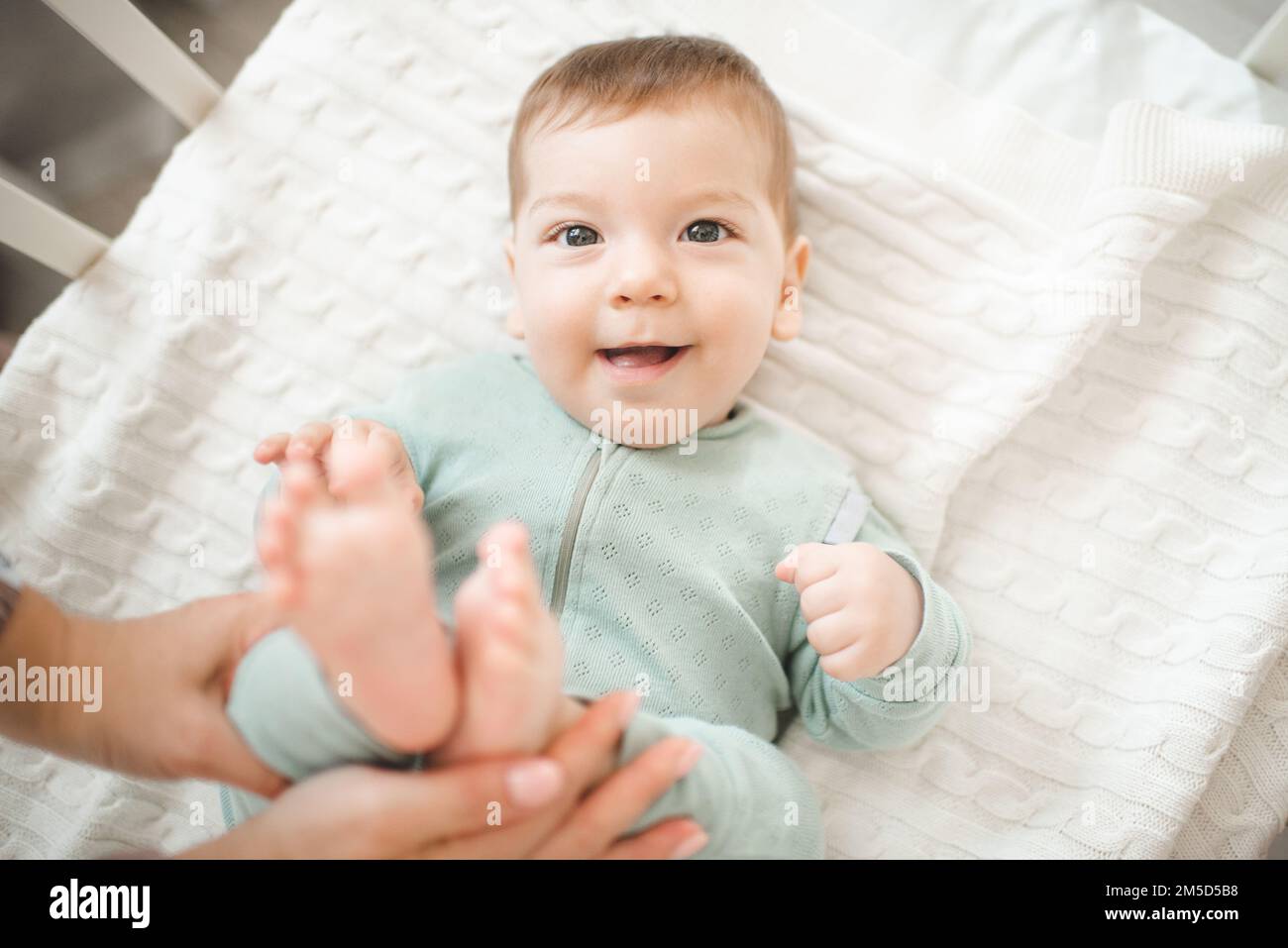 Funny smiling infant baby boy wake up in bed crib over white blanket
