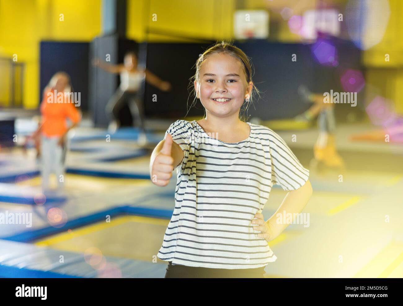 Cheerful tween girl giving thumbs up on trampolines in inflatable ...