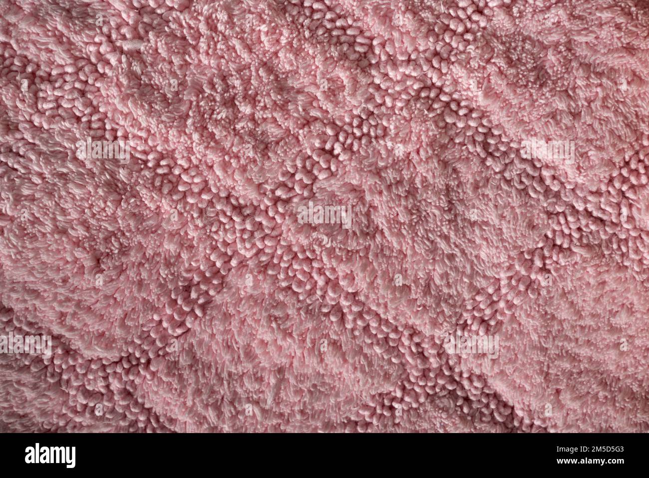 Fragment of decorative carpet fabric pattern, textured background. Close up of pink short pile carpet, with geometric barely noticeable rhombus ornament. Concept of backgrounds and textures. Stock Photo