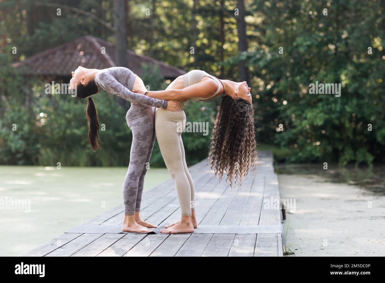 Two women leading a healthy lifestyle and practicing yoga, performing holding on to each other the exercise of Hasta Uttanasana, a posture of deflecti Stock Photo