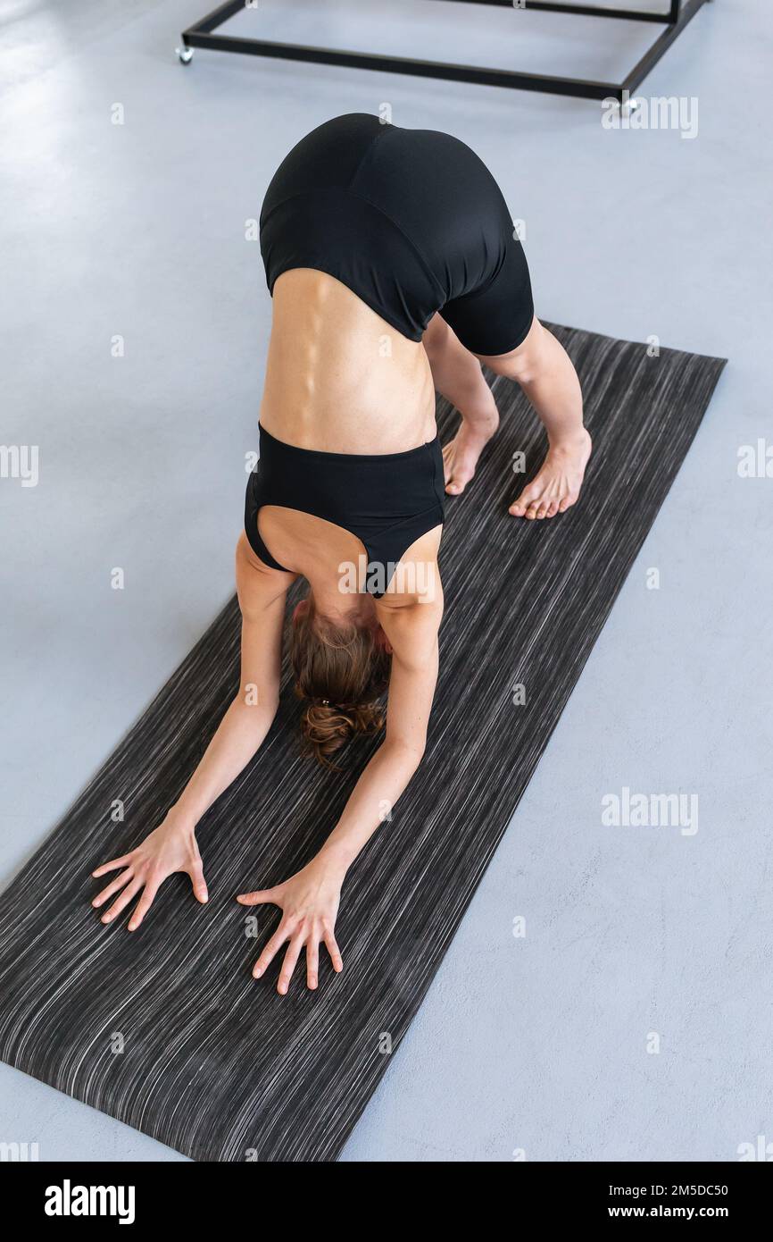 Young woman leading a healthy lifestyle and practicing yoga, performs Ardha Pincha Mayurasana exercise, dolphin pose, exercising in black sportswear i Stock Photo