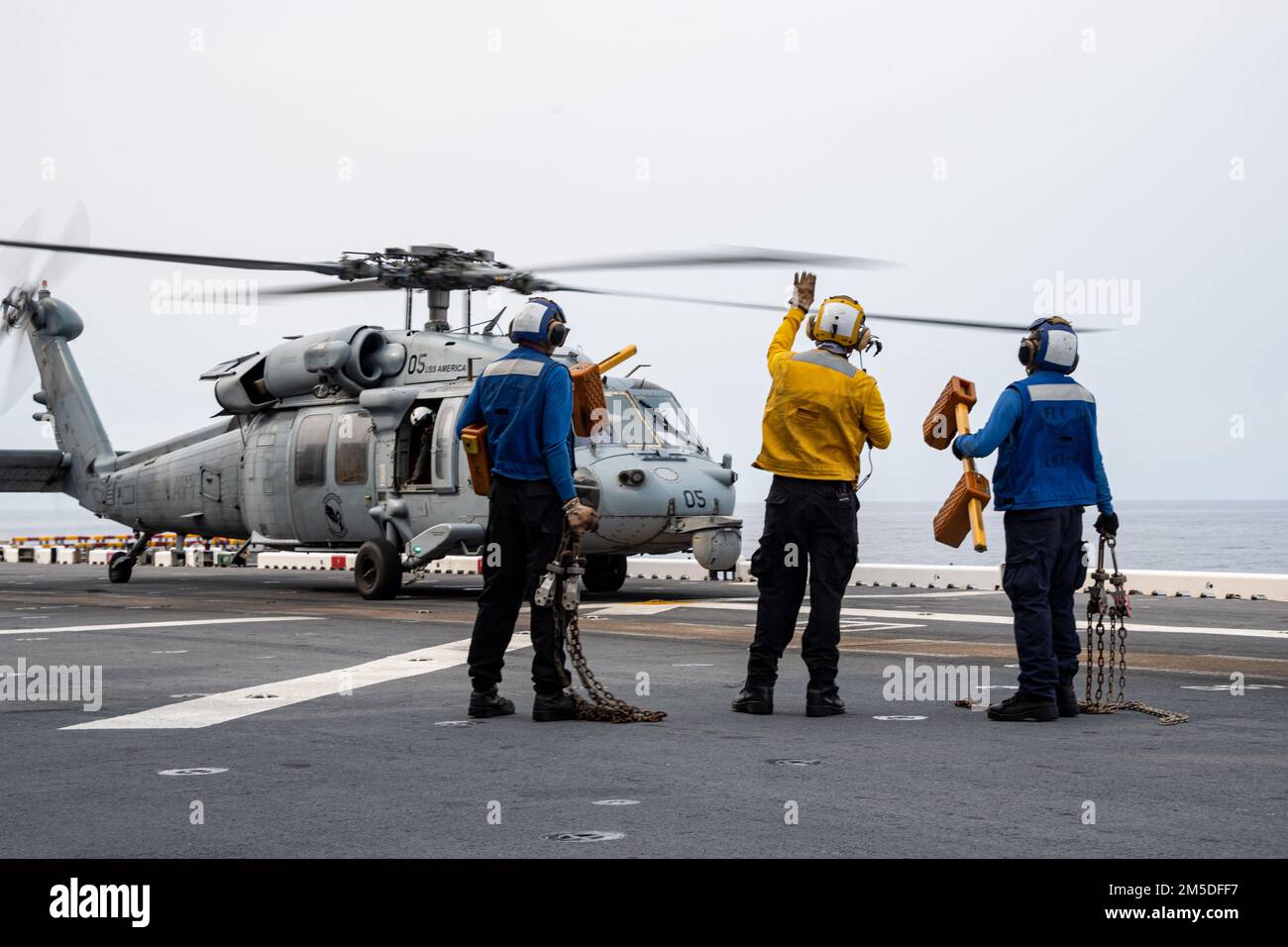 PHILIPPINE SEA (March. 4, 2022) Sailors assigned to the forward-deployed amphibious assault ship USS America (LHA 6) signal that chocks and chains were removed from an MH-60S Sea Hawk helicopter from Helicopter Sea Combat Squadron (HSC) 25 on the ship’s flight deck. America, lead ship of the America Amphibious Ready Group, along with the 31st Marine Expeditionary Unit, is operating in the U.S. 7th Fleet area of responsibility to enhance interoperability with allies and partners and serve as a ready response force to defend peace and stability in the Indo-Pacific region. Stock Photo