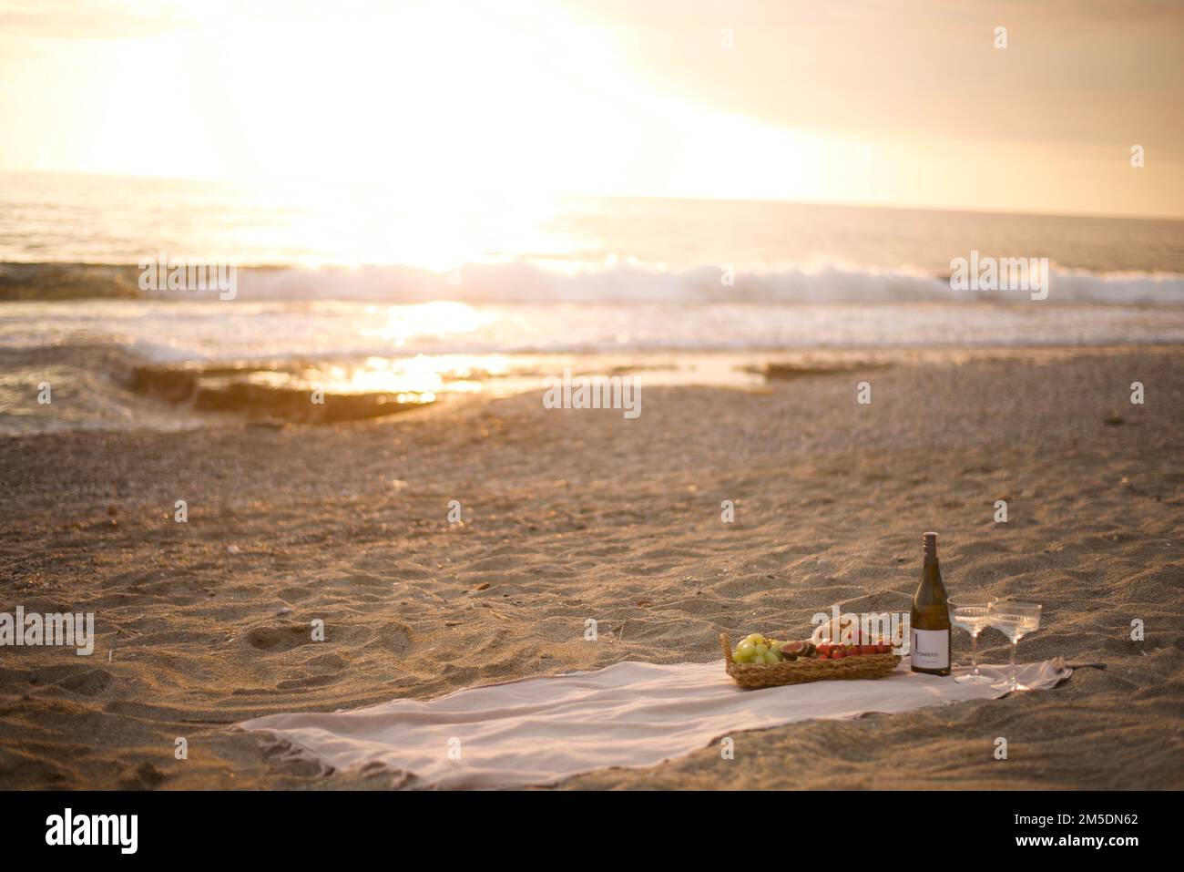 Romantic picnic by the sea at sunset Deserted beach in the warm rays of sunset Champagne and fruit basket Stock Photo