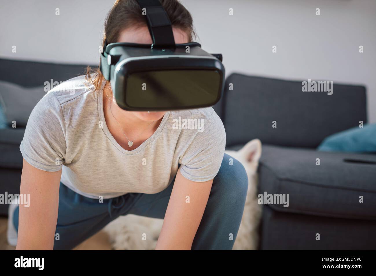 Caucasian young woman having a workout in VR headset, doing arm stretching exercises at home. Sport, health, and virtual reality concept. Stock Photo