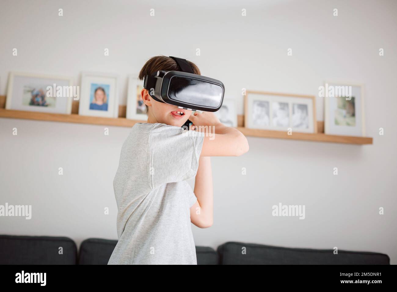 Boy child playing swordplay video games at home, wearing virtual reality vr headset and holding remote controller Stock Photo