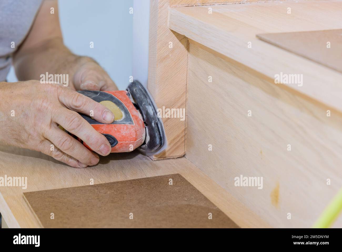 Grinding carpenter using polishing machine to refinish new home stairwell railings trims Stock Photo