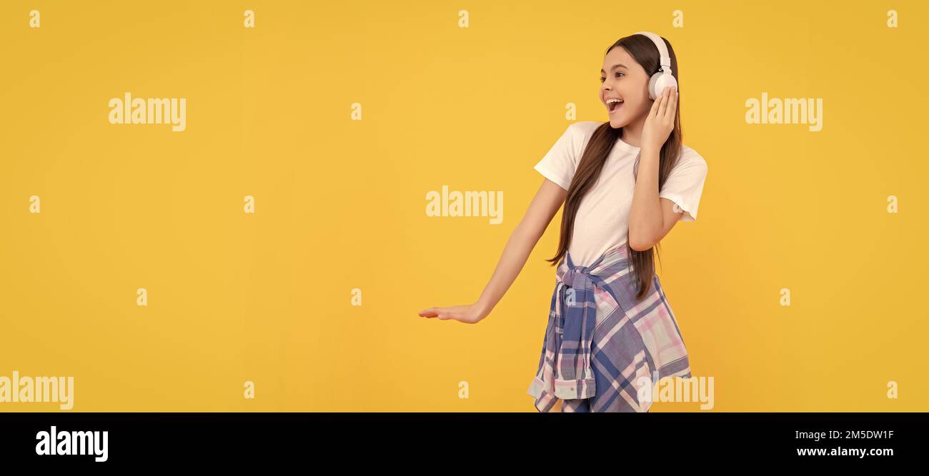 Happy teen girl in headphones singing along to song yellow background. Child portrait with headphones, horizontal poster. Girl listening to music Stock Photo