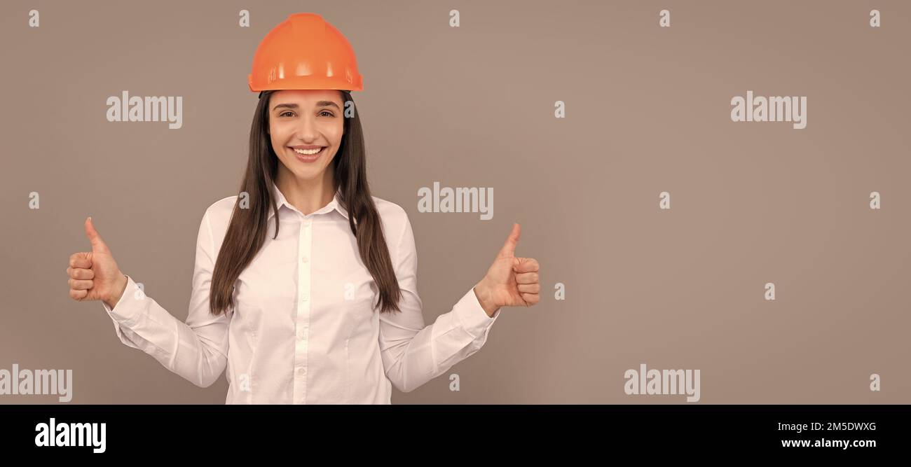 happy woman in protective helmet and white shirt showing thumb up gesture, good result. Woman isolated face portrait, banner with mock up copy space. Stock Photo